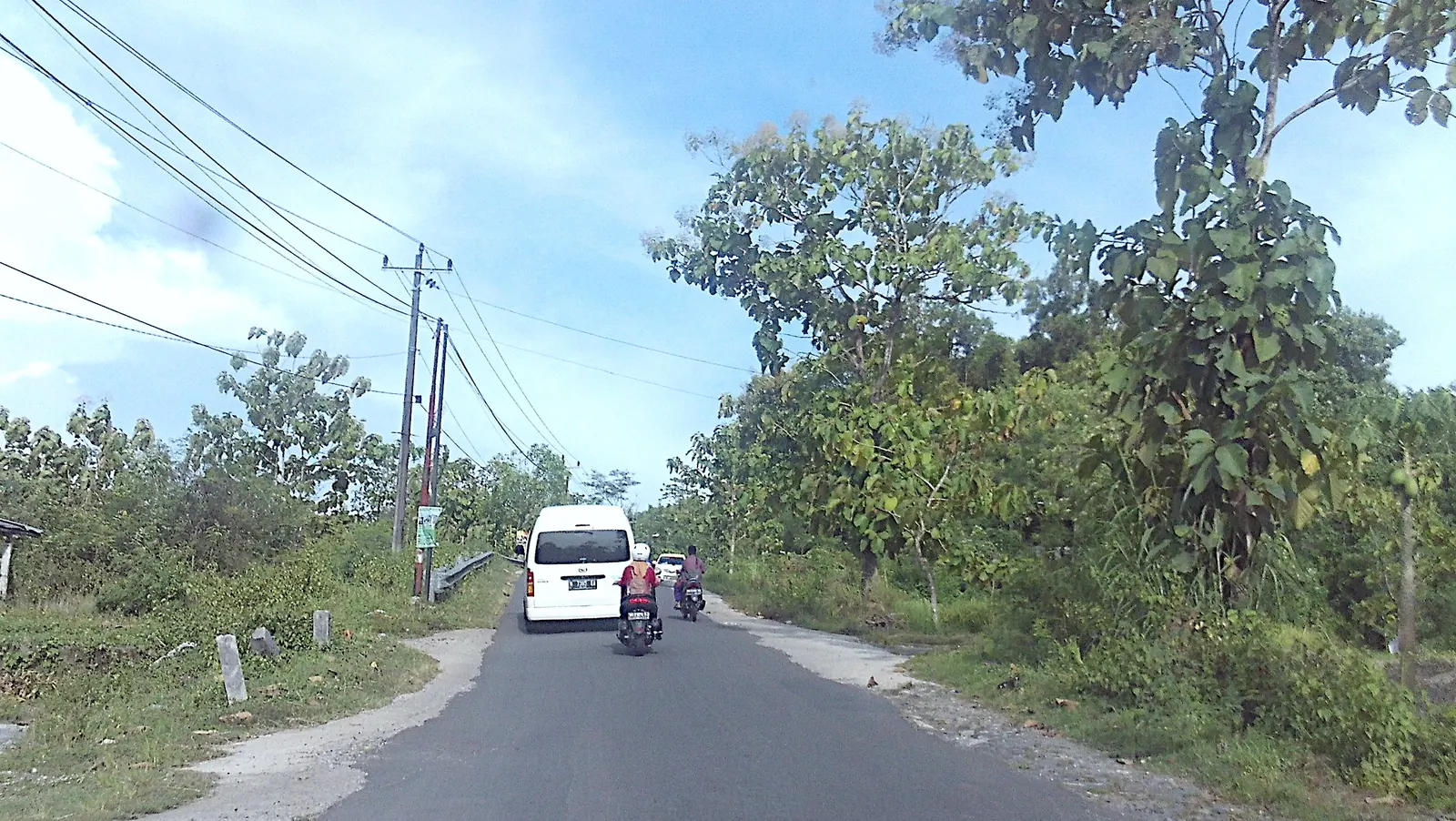Mobil dan sepeda motor di Jalan Candi Ijo dengan pepohonan dan jaringan utilitas di sisi jalan